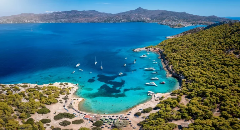 Vista aerea panoramica della popolare spiaggia dell'isola di Moni, vicino al villaggio di Perdika sull'isola di Egina con il mare turchese, Golfo Saronico, Grecia